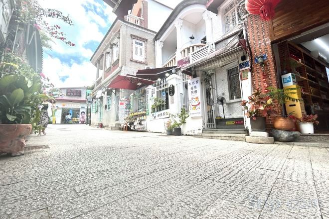A street with buildings, potted plants, and a tiled pavement.
