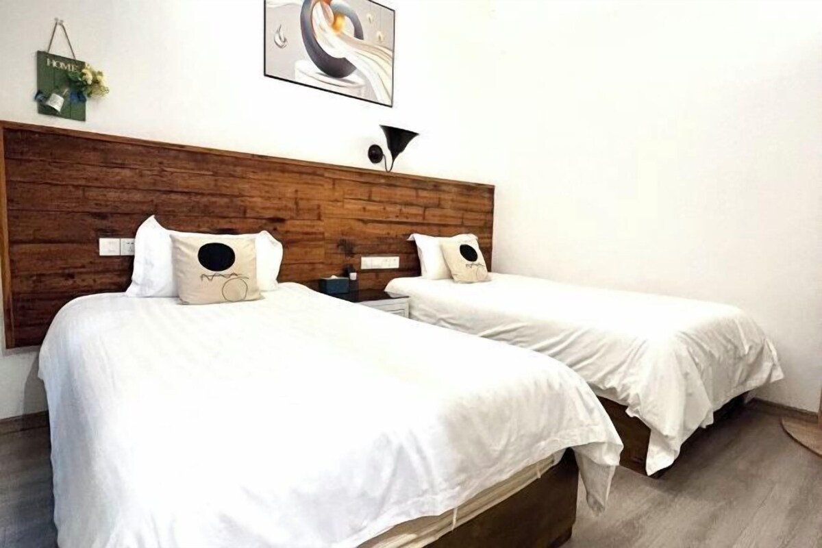 A hotel room with two beds, wooden headboard, white bedding, and a wall-mounted artwork.