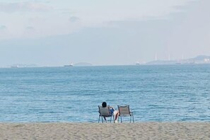 A beach with two chairs facing the sea, a distant ship, and a hazy horizon. - Mumujia Homestay (Xiamen)