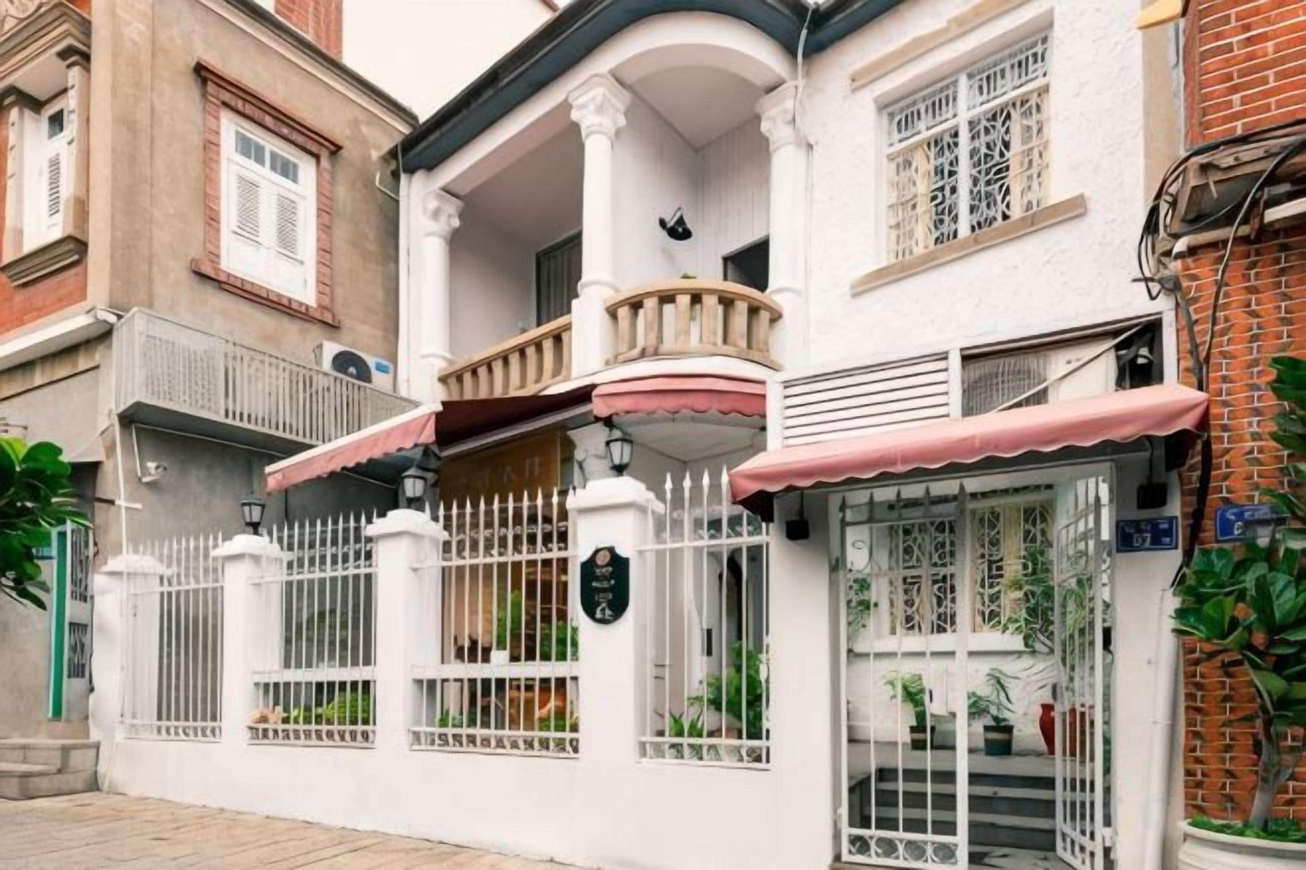 Un edificio de dos pisos con balcón, entrada protegida por una reja y ventana con vista a la calle.