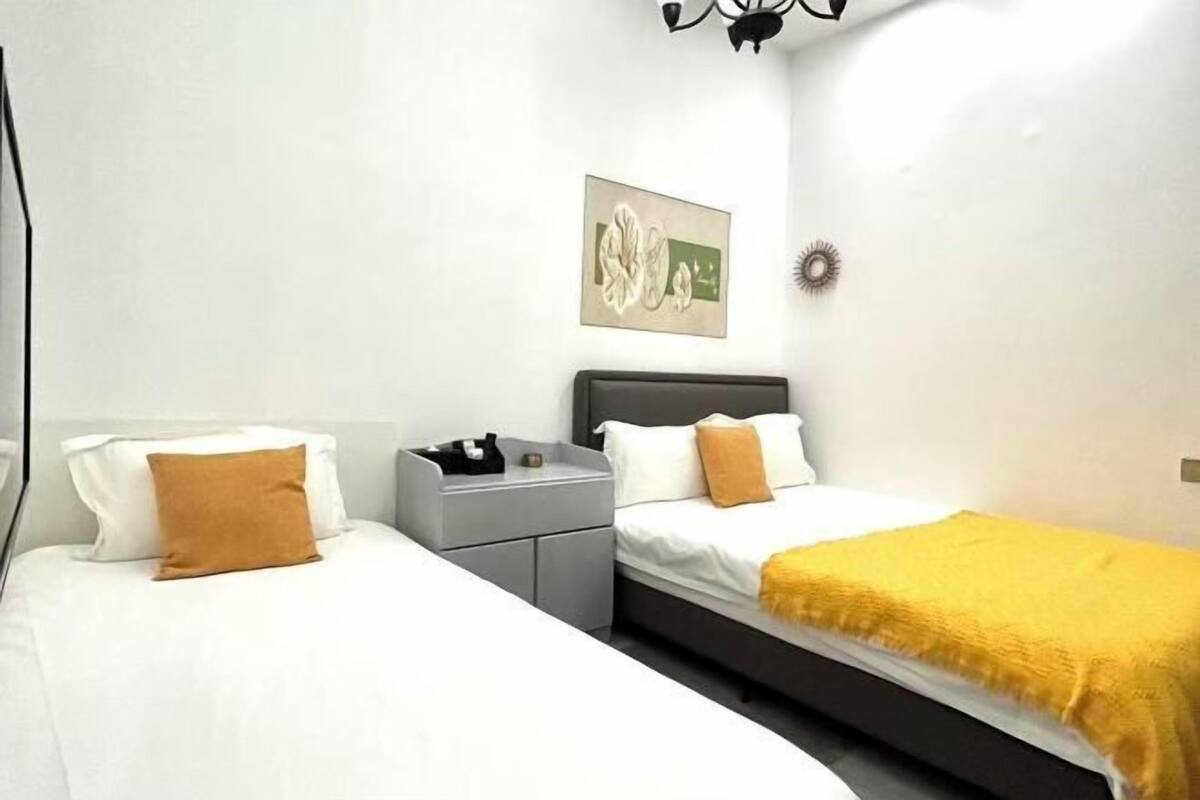 A bedroom with two beds, a nightstand, a wall-mounted artwork, and a ceiling light fixture.