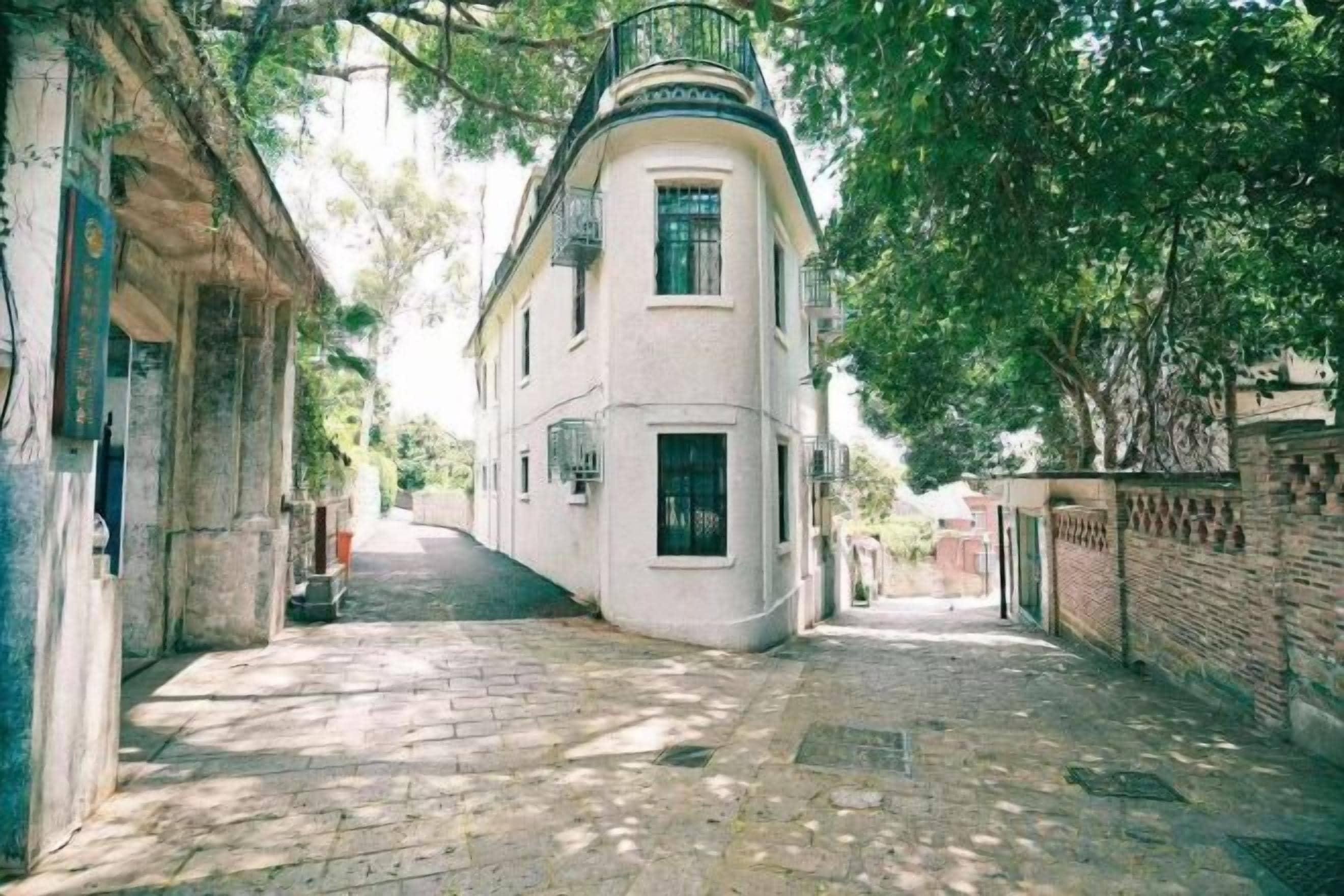 A narrow cobblestone street flanked by buildings with balconies and a brick wall on one side.