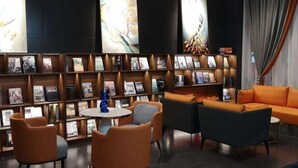 Uma área de estar moderna com um sofá, cadeiras e uma estante cheia de revistas e livros.