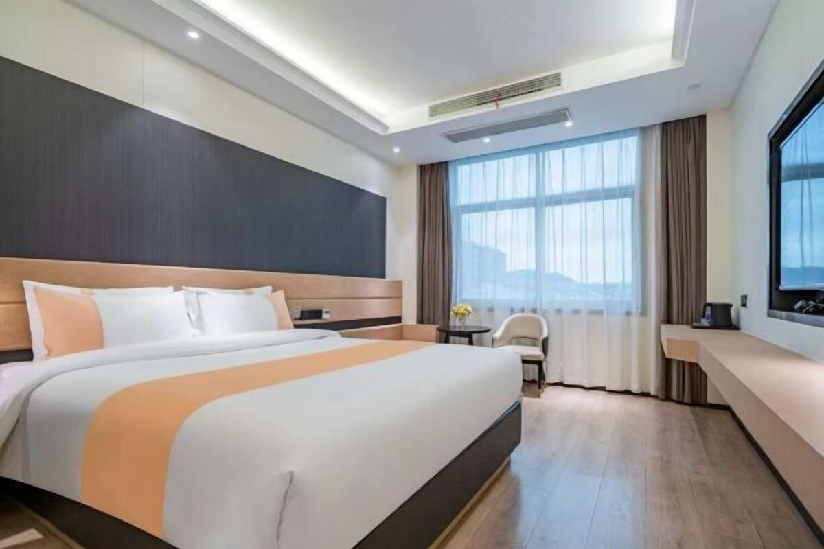 A modern hotel room with a large bed, a desk, and a view of the city.