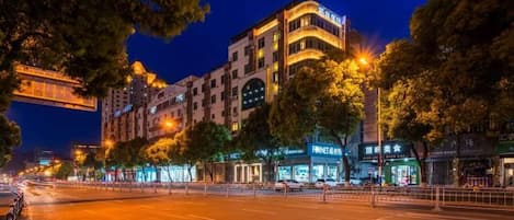 A multi-story building with illuminated signage, a wide street, and trees.