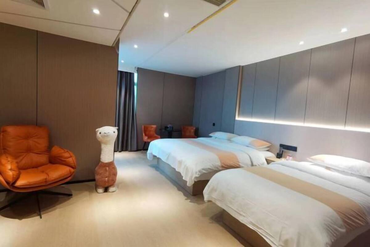 A modern hotel room with a large bed, a smaller bed, a sofa, and a chair.