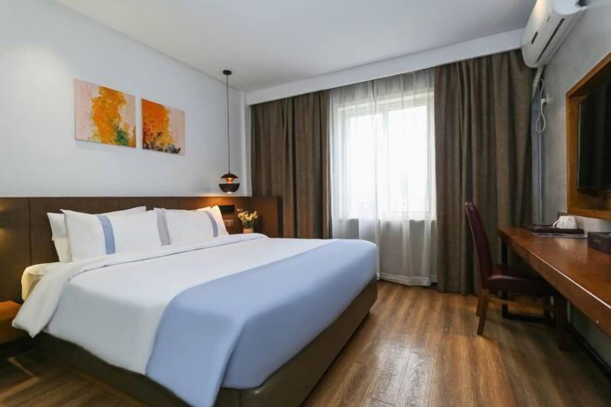A hotel room with a bed, a desk, a chair, a TV, and a window with curtains.
