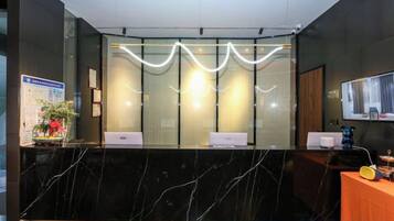 A reception desk with a marble countertop, a glass partition, and a modern light fixture above.
