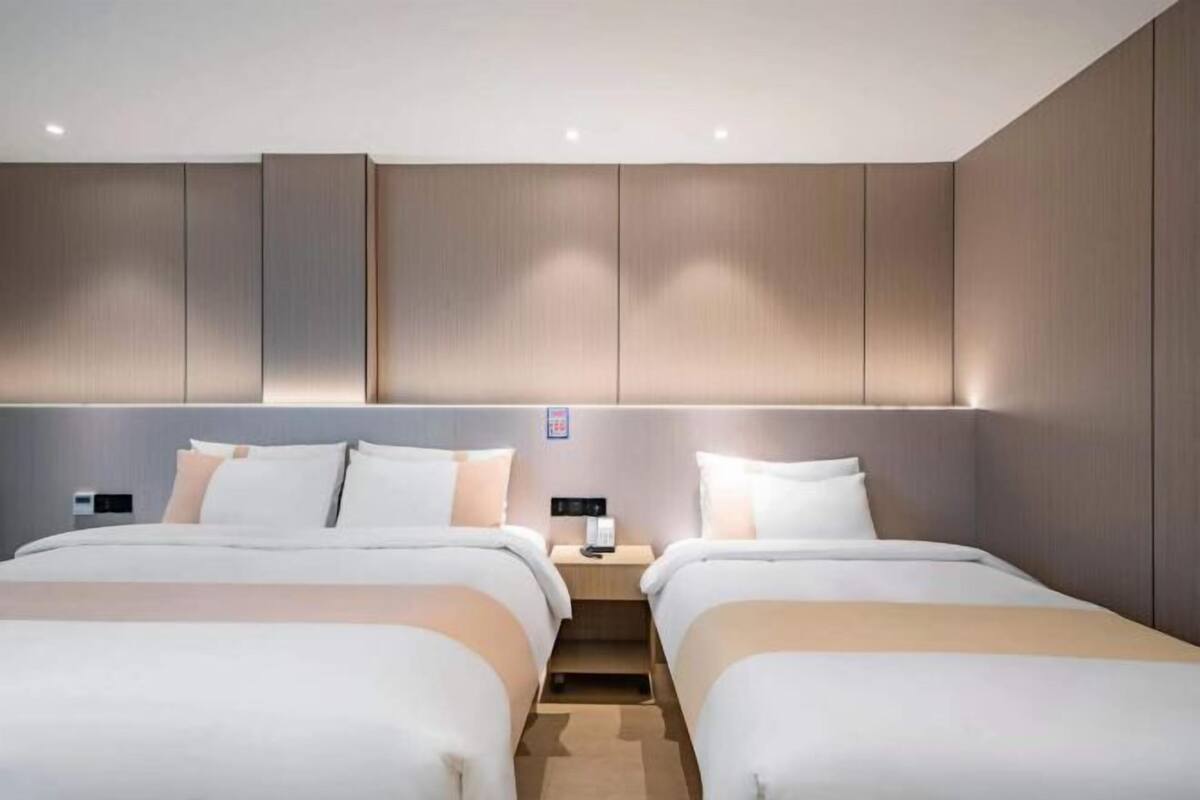 A hotel room with two beds, a nightstand, and a wall-mounted light fixture.