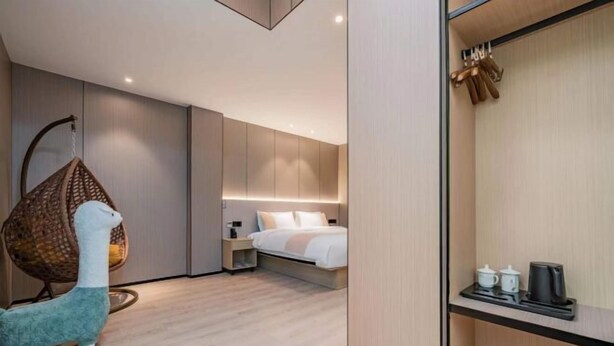 Quarto de hotel moderno com cama, mesa de cabeceira, cadeira suspensa e prateleira com chávenas e chaleira.