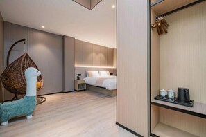 Moderni hotellihuone, jossa on sänky, yöpöytä, riipputuoli sekä hylly, jossa on kuppeja ja vedenkeitin.
