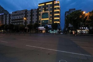 Un edificio de varios pisos con señalización iluminada, una calle ancha en primer plano y un cielo despejado.