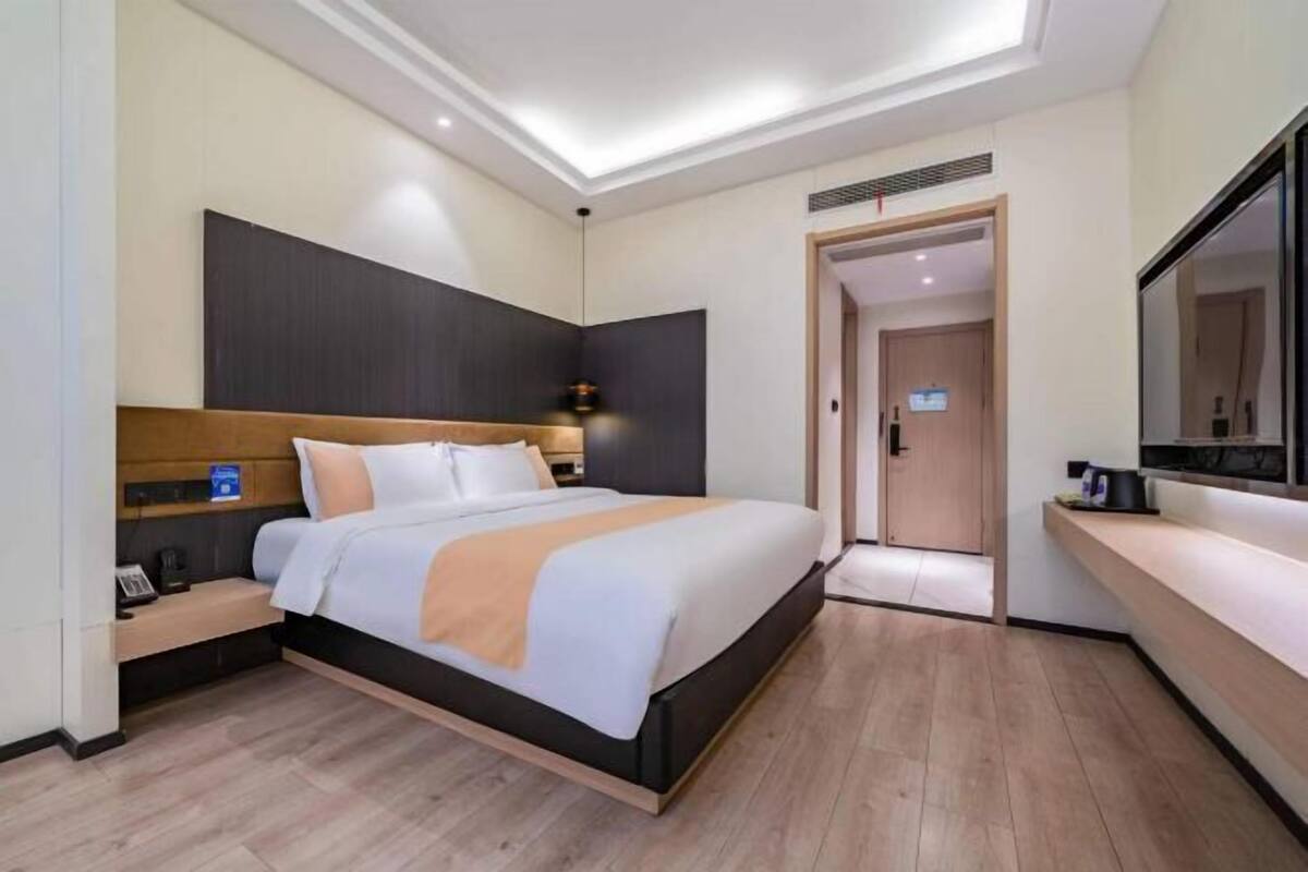 A modern hotel room with a large bed, a bedside table, a nightstand, a built-in TV, and a mirror on the wall.