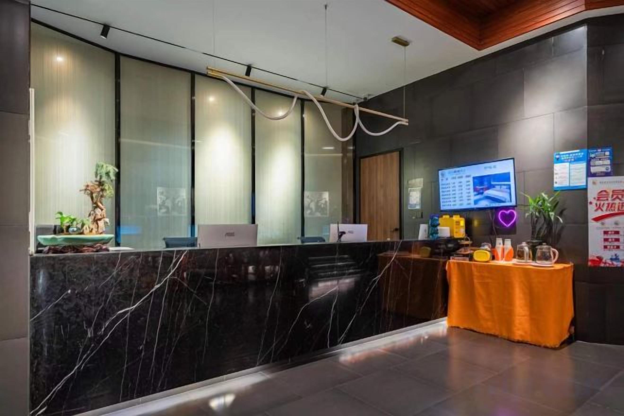 A reception area with a marble counter, a computer, a small table with a plant, and a wall-mounted TV.