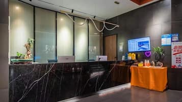 A reception area with a marble counter, a computer, a small table with a plant, and a wall-mounted TV.