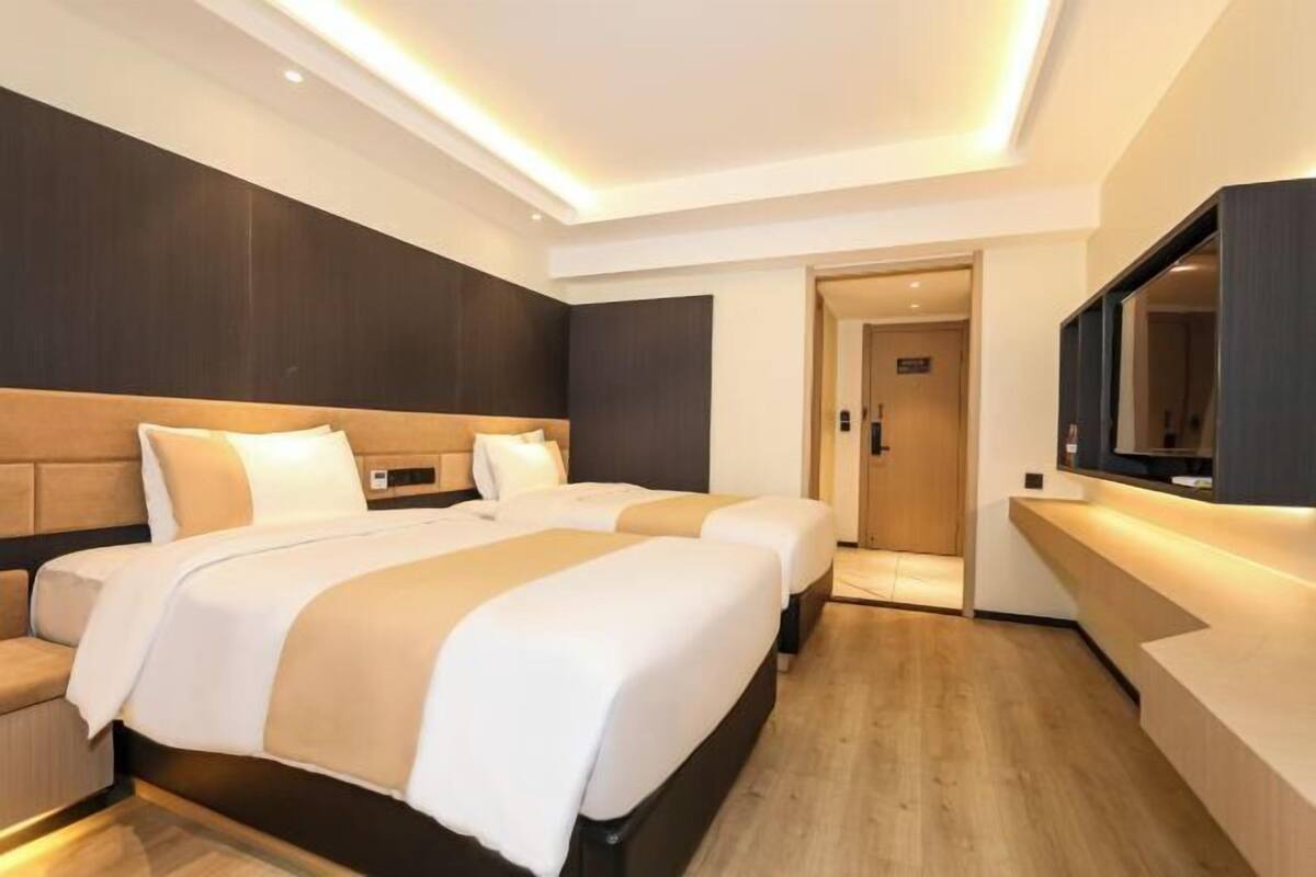 A modern hotel room with two beds, a flat-screen TV, and a wooden floor.