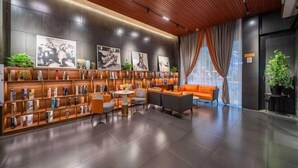 Um hall moderno com teto de madeira, uma estante grande, área de estar com sofás laranja e janelas amplas com cortinas.