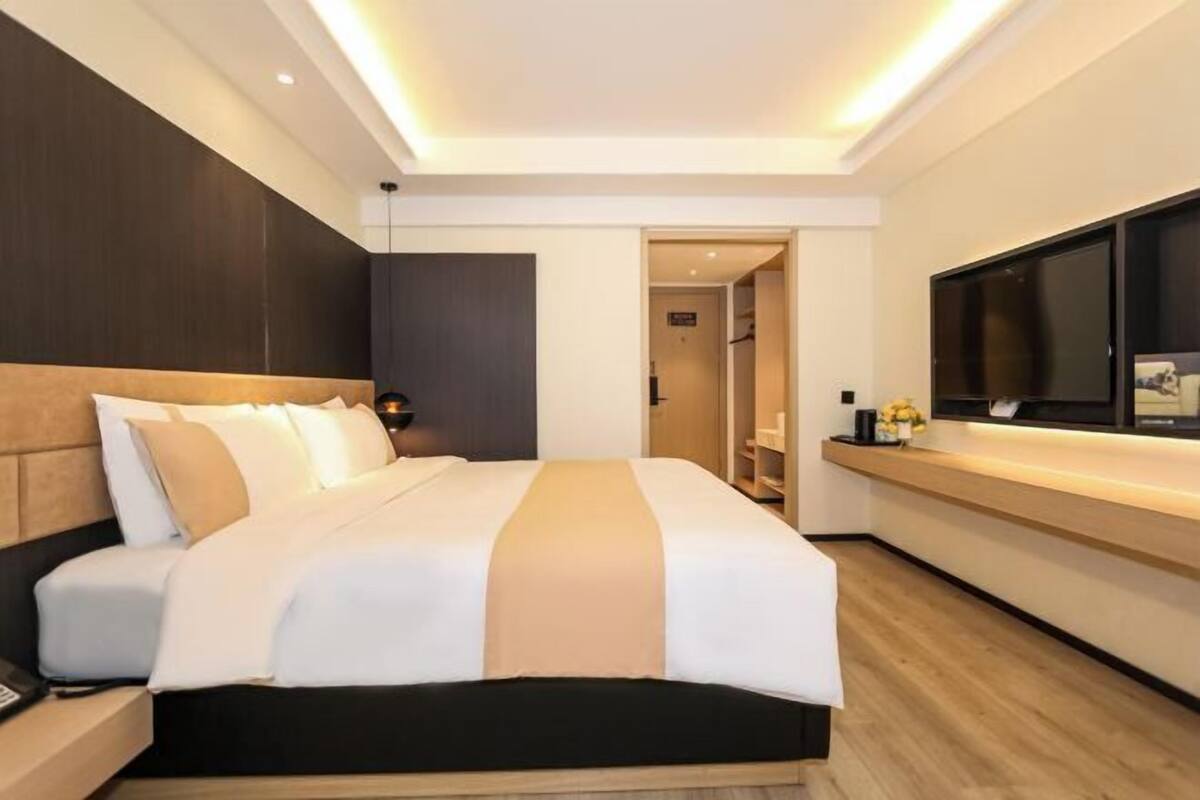 A modern hotel room with a large bed, a flat-screen TV, and a wooden floor.