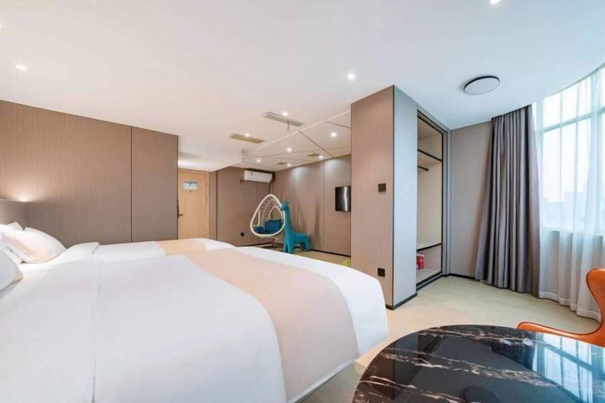 A modern hotel room with a large bed, a hanging chair, and a glass table.
