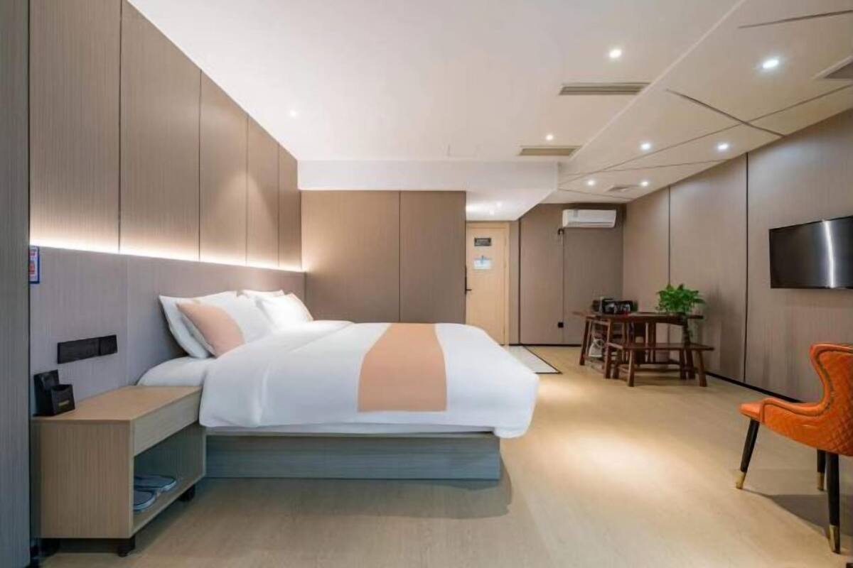 A modern hotel room with a bed, bedside table, TV, and a dining area with chairs and a table.