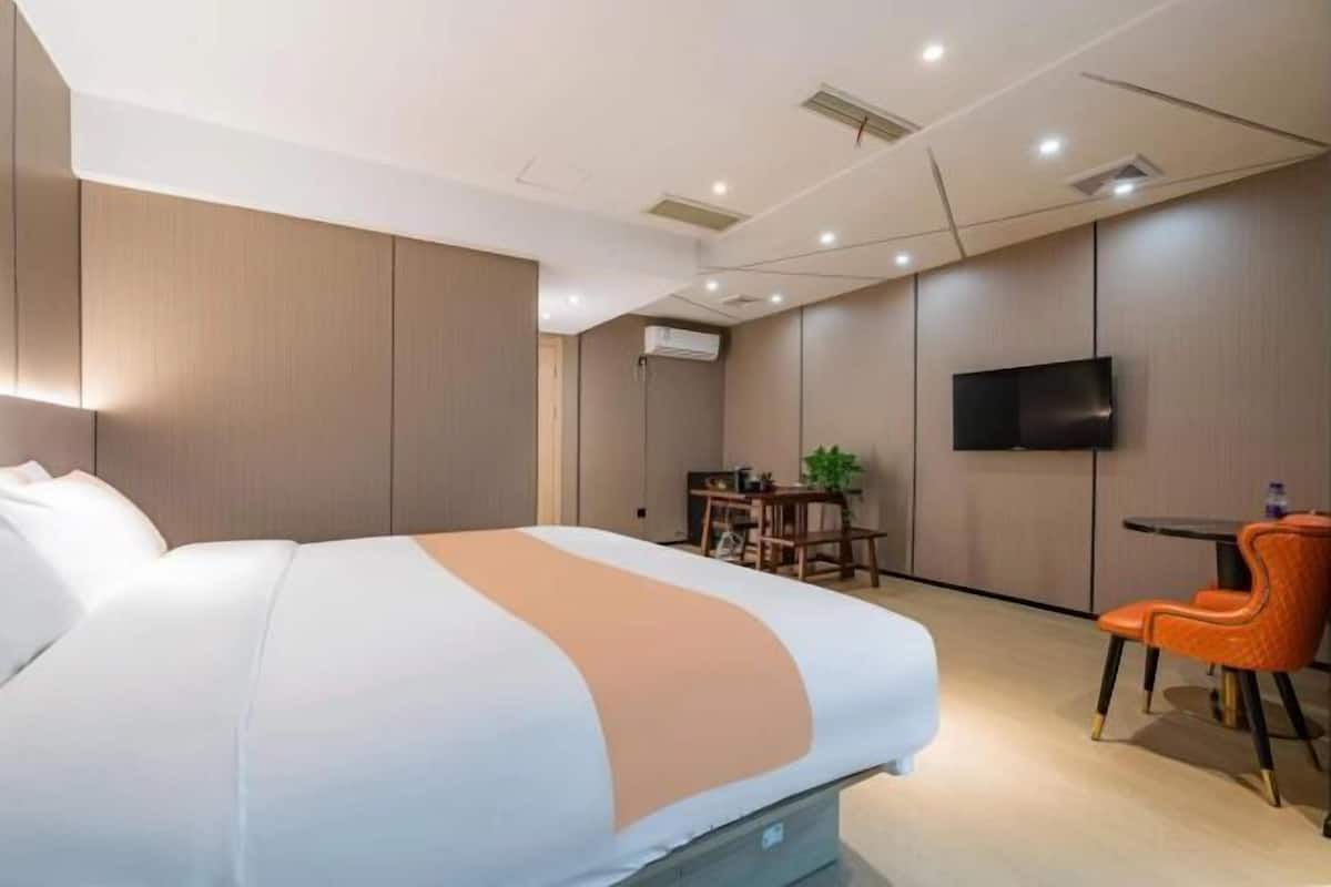 A hotel room with a bed, a desk, a chair, a television, and an air conditioning unit.