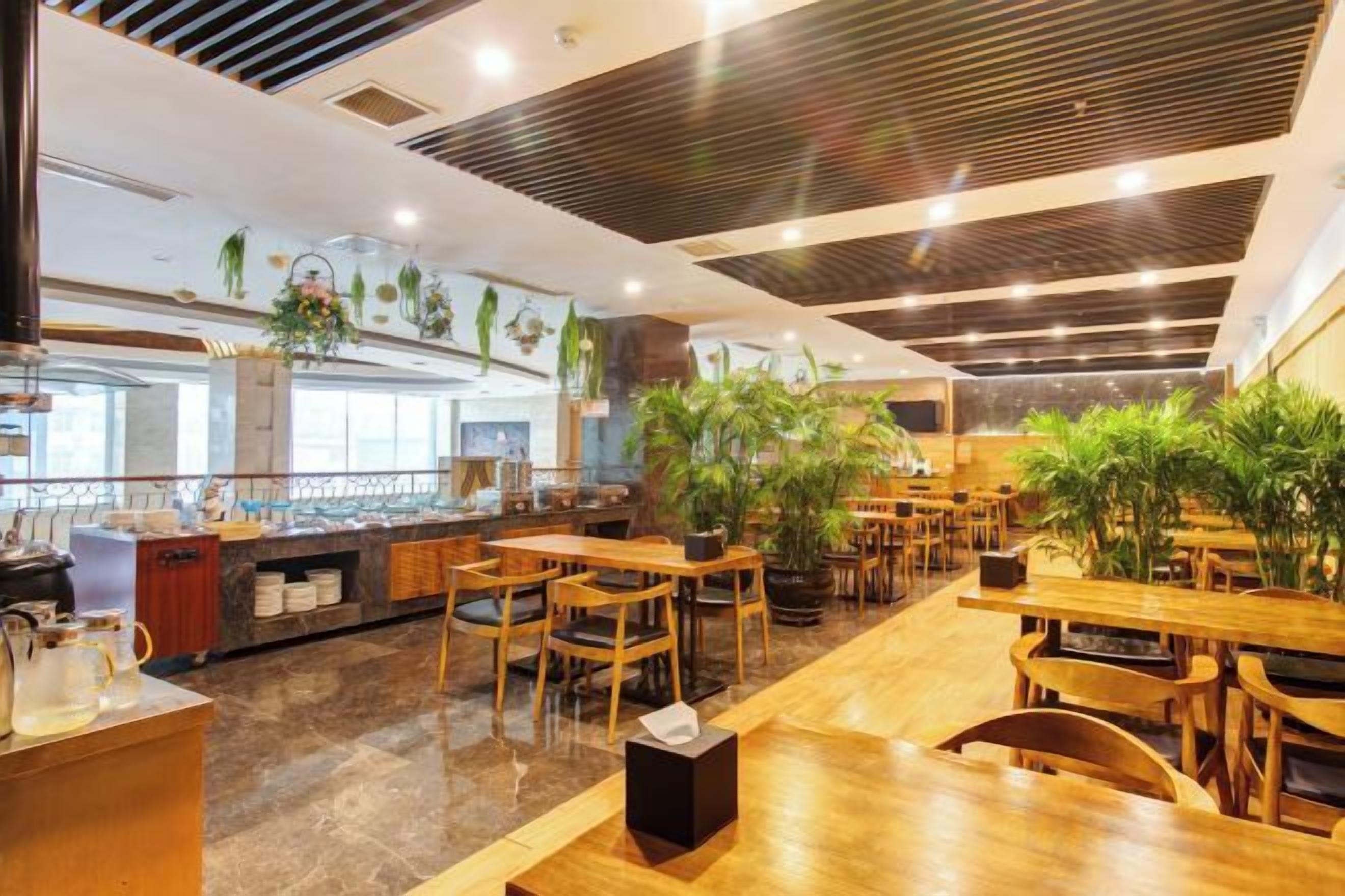 A restaurant with wooden tables and chairs, a kitchen area, and potted plants.