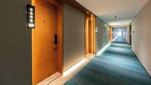 Un pasillo de hotel con alfombra azul, puertas de madera y letreros iluminados.