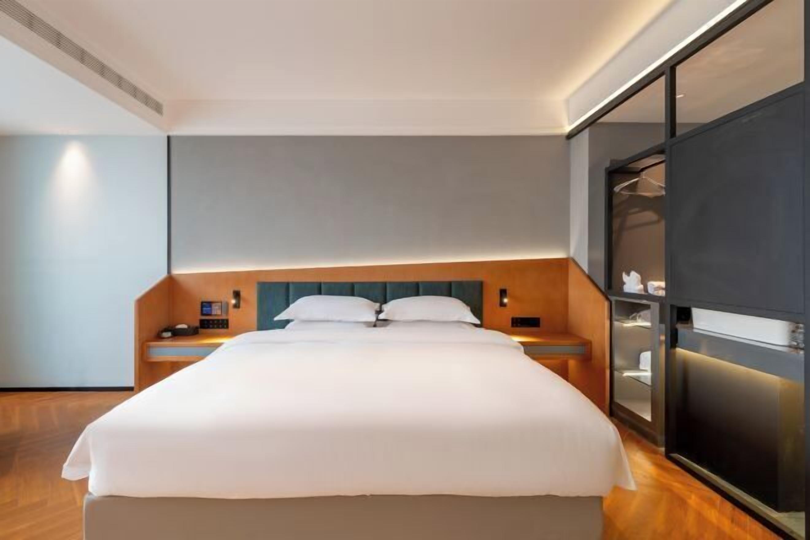 A modern hotel room with a large bed, wooden headboard, bedside tables, and a built-in wardrobe.