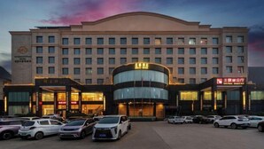 Un hotel de varios pisos con un atrio central, múltiples espacios de estacionamiento y una entrada destacada con señalización iluminada.