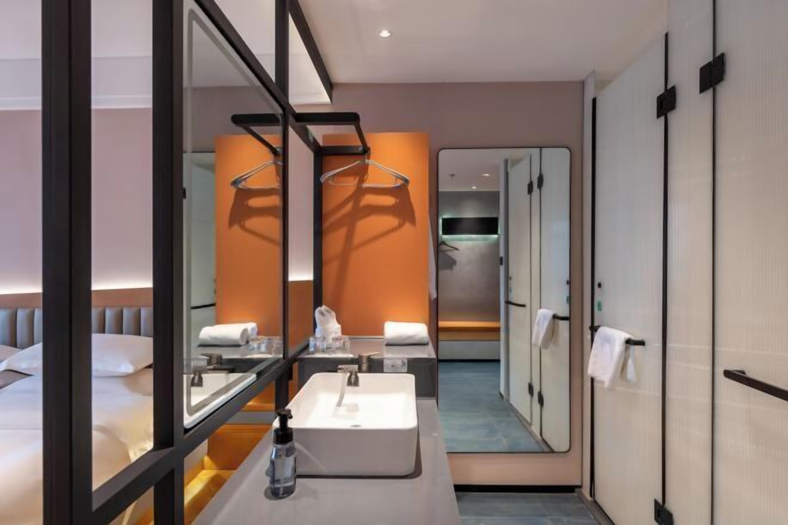 A modern hotel room with a large bed, a bathroom with a mirror, and a walk-in closet.