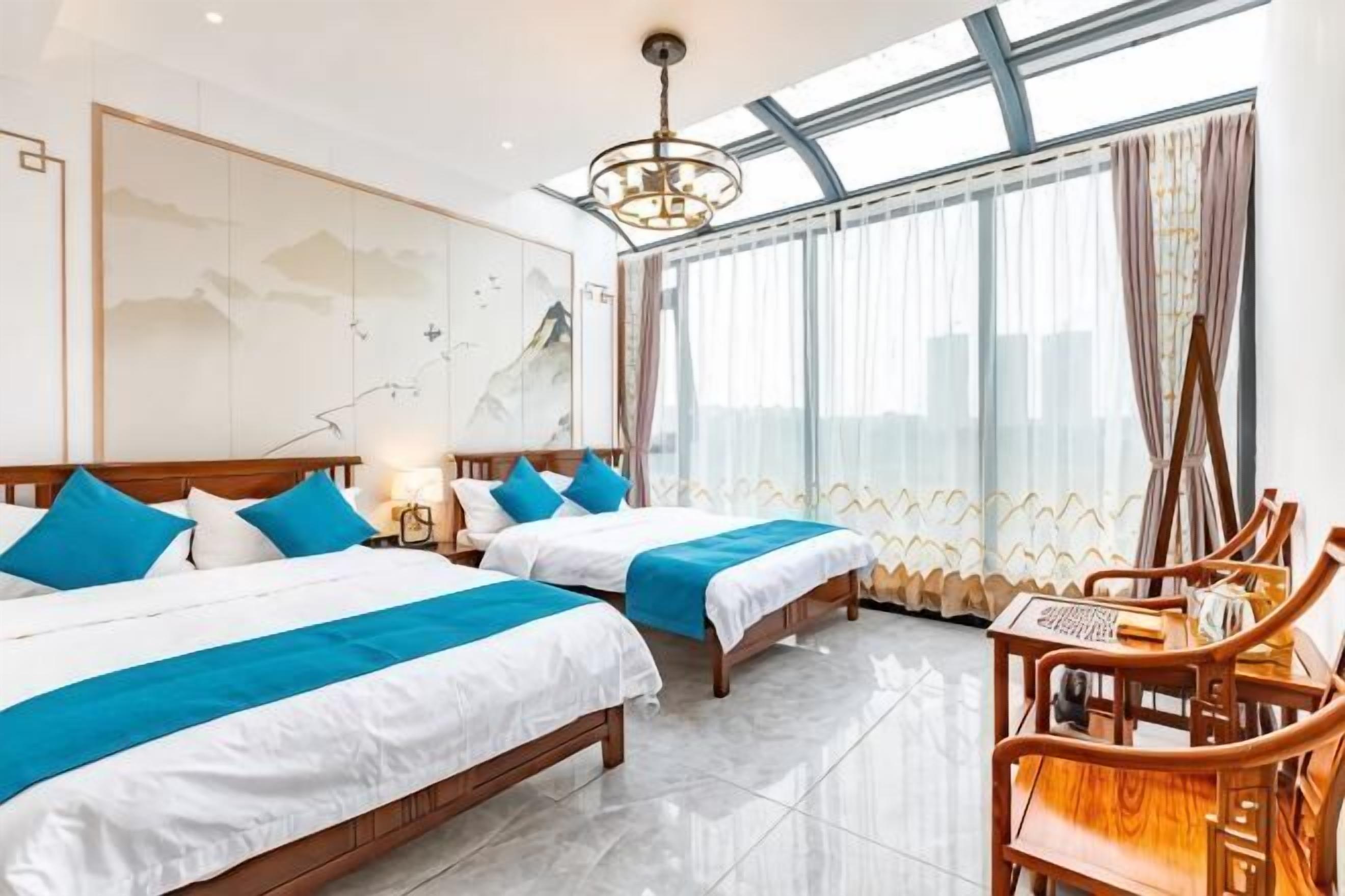 Una habitación de hotel con dos camas, una silla de madera, un ventanal grande y un candelabro.