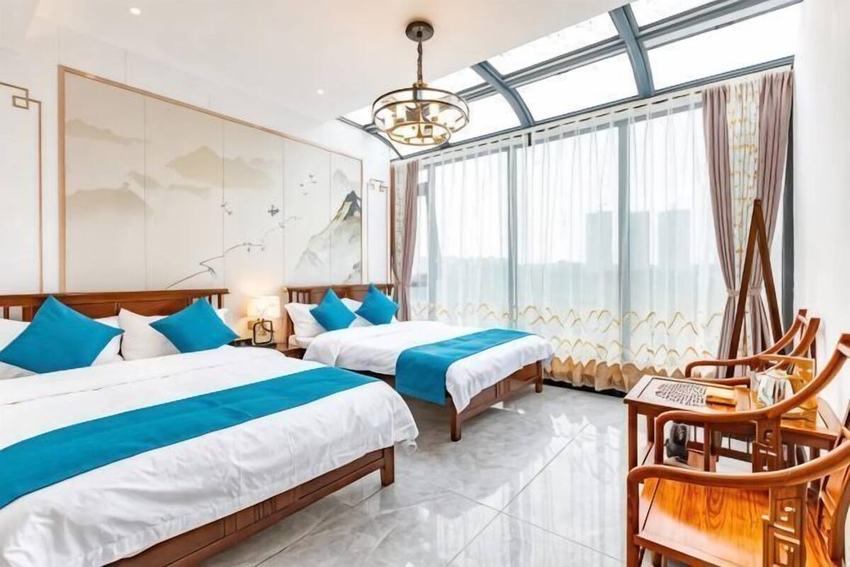 Een hotelkamer met twee bedden, een houten stoel, een groot raam en een kroonluchter.