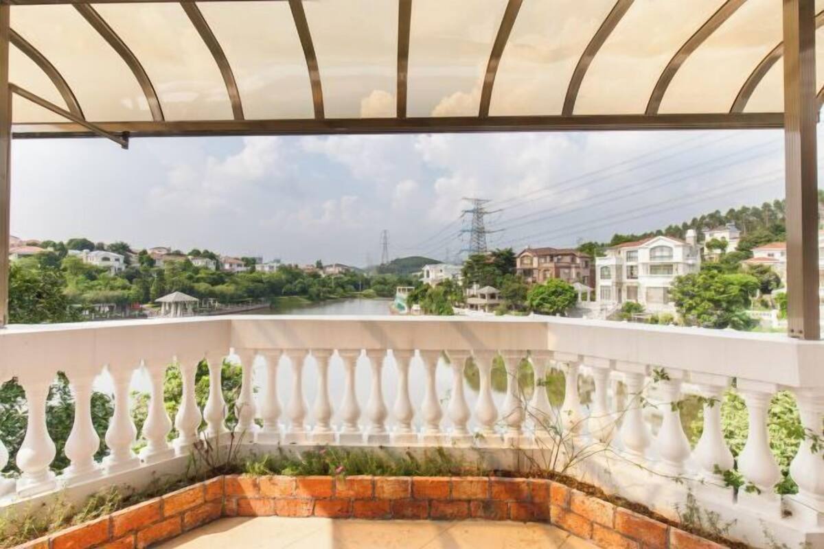 Een balkon met uitzicht op een woonwijk, een bakstenen muur en een witte balustrade.
