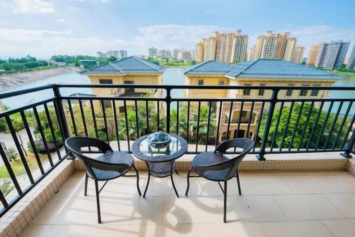 Een balkon met twee stoelen en een tafel, met uitzicht op een rivier en hoge gebouwen.