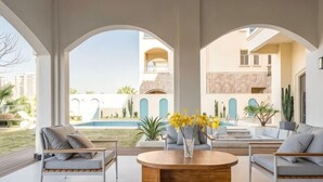 A modern living room with a pool view, featuring a round wooden coffee table, grey sofas, and a large arched window.