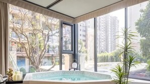 A room with a large window, a hot tub, and a potted plant.
