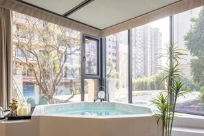 Quarto com uma grande janela, banheira de hidromassagem e uma planta em vaso.