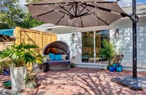 Un patio con zona de estar cubierta, plantas en macetas y un paraguas grande.