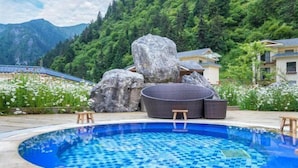 Une piscine aux carreaux de mosaïque, entourée de gros rochers et de mobilier d’extérieur.