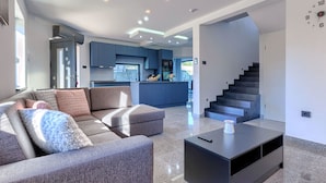 A modern living room with a grey sofa, a black coffee table, and a kitchen area with blue cabinets and a central island.