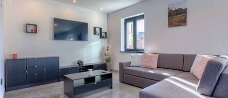 A modern living room with a grey sofa, a flat-screen TV, and a dark wooden cabinet.