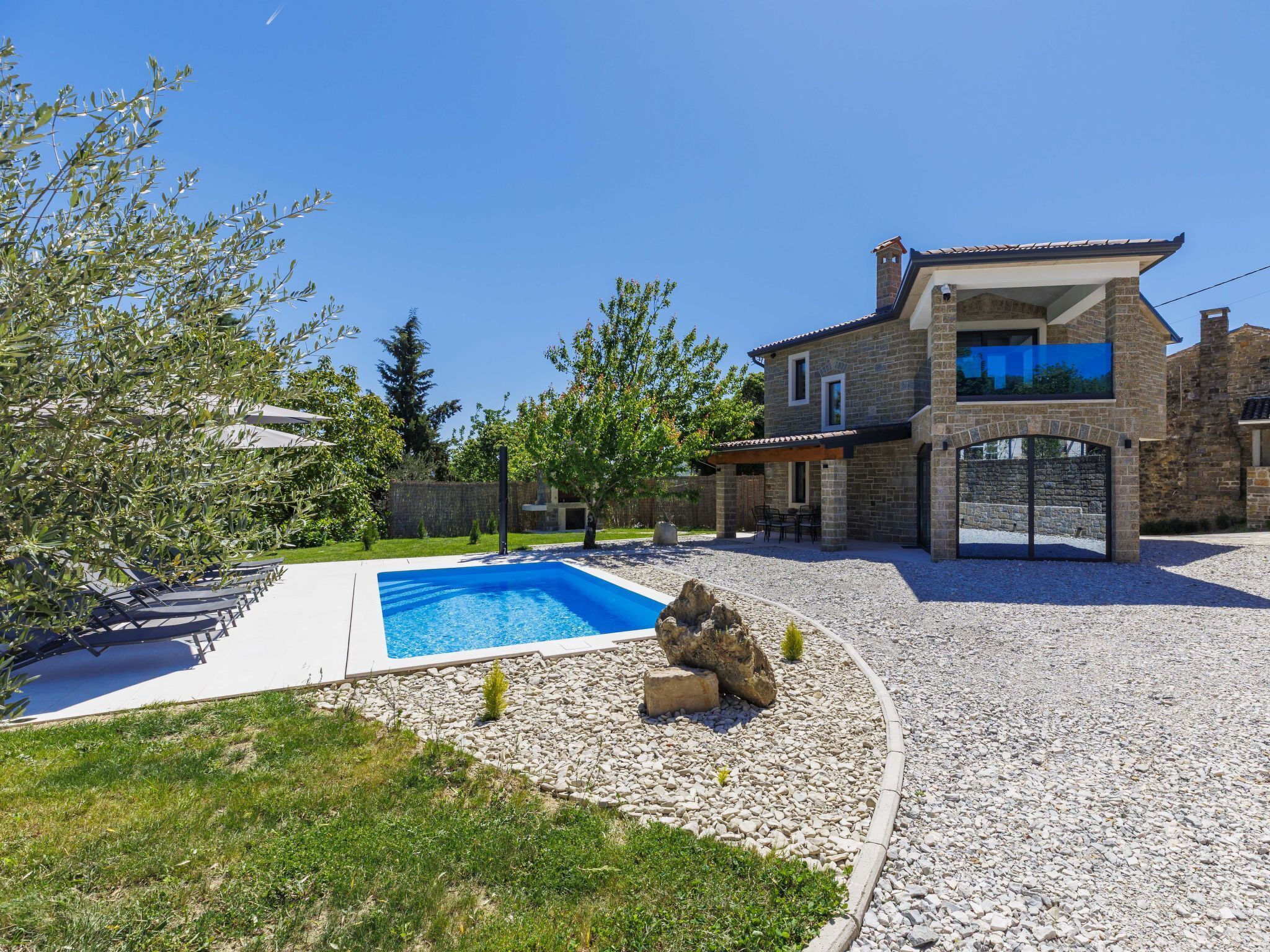 Una casa de piedra de dos pisos con piscina, mobiliario exterior y una entrada de piedra.