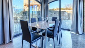 A modern dining area with a glass table, black chairs, and a view of a stone building through large windows.