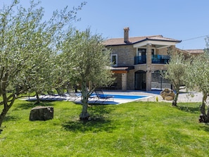 Une maison en pierre à deux étages, dotée d’une piscine, d’un espace salon extérieur et d’oliviers.