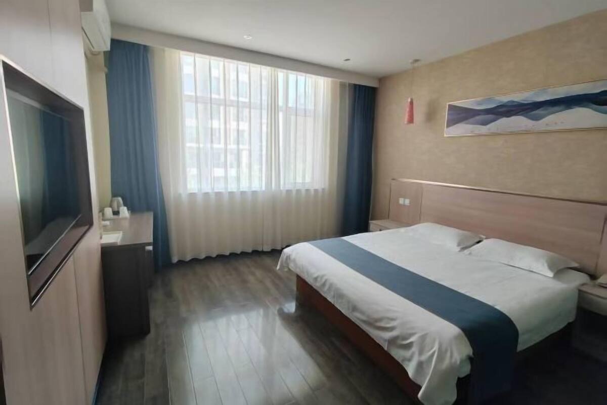 Une chambre d’hôtel avec un lit, un bureau, une télévision et une fenêtre avec des rideaux.