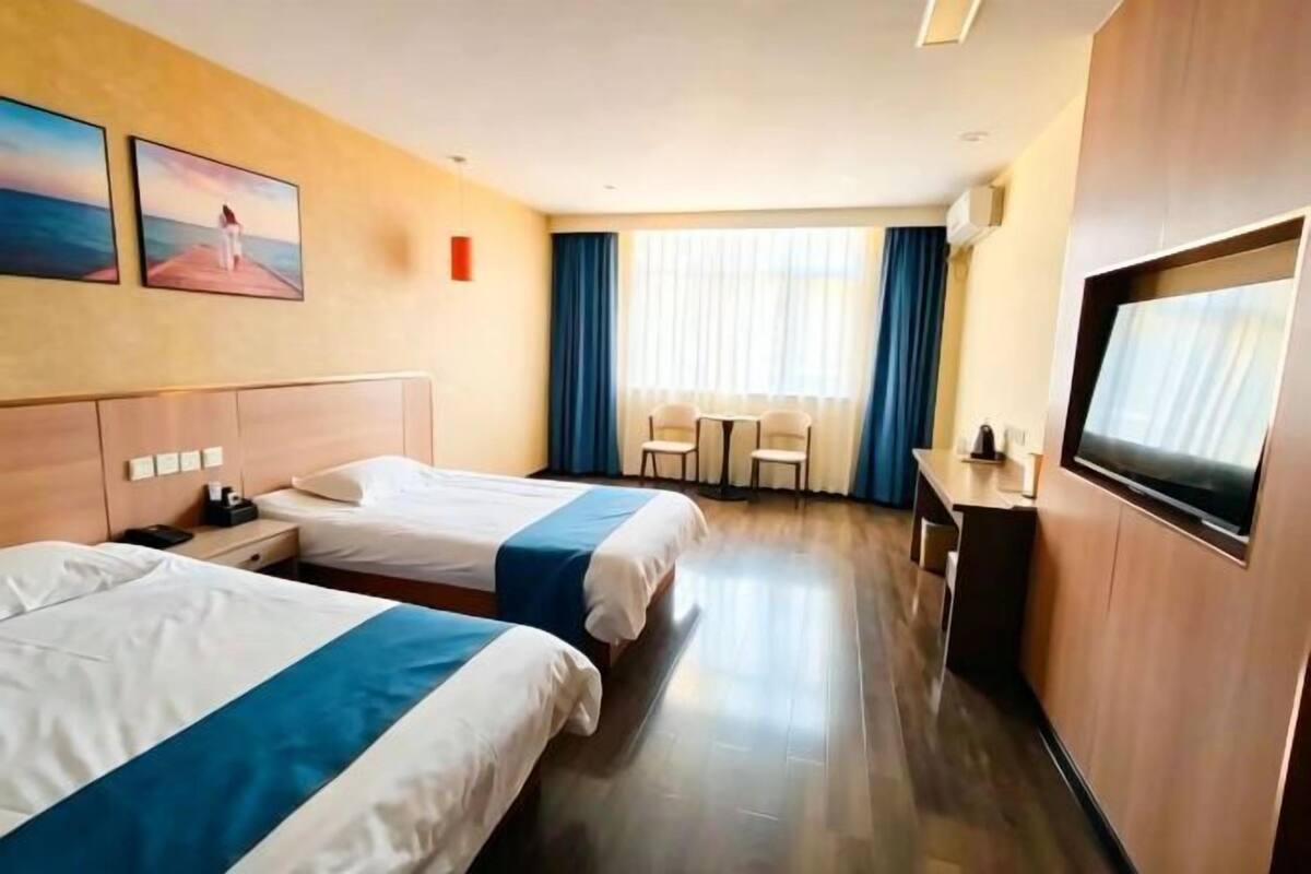 Une chambre d’hôtel avec deux lits, une télévision, un bureau et une fenêtre avec des rideaux.
