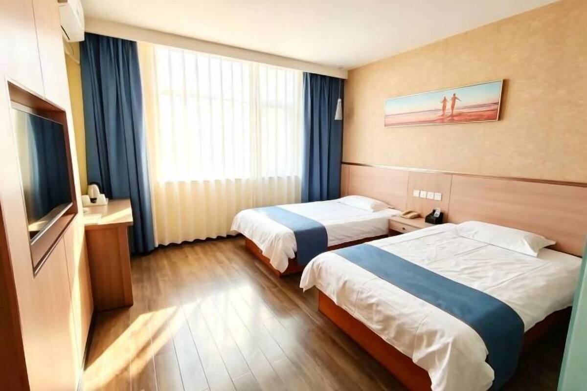 Une chambre d’hôtel avec deux lits, un bureau, une chaise, une télévision et un tableau au mur.