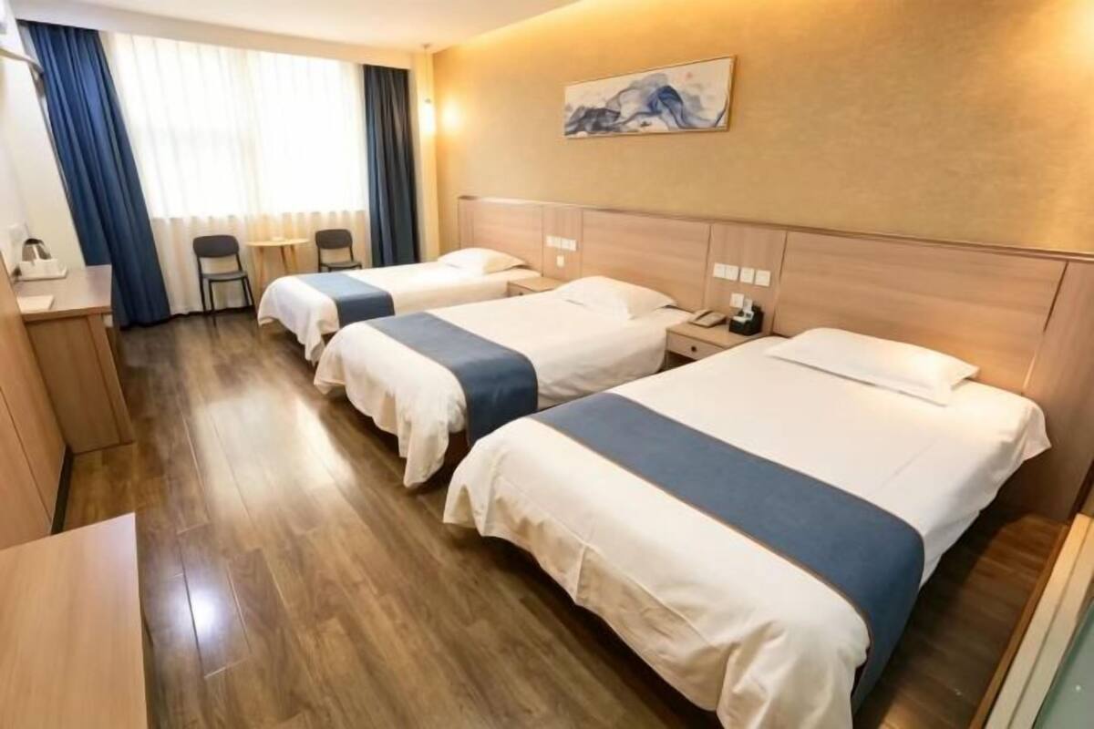 Une chambre d’hôtel avec trois lits, un bureau, des chaises et un tableau au mur.