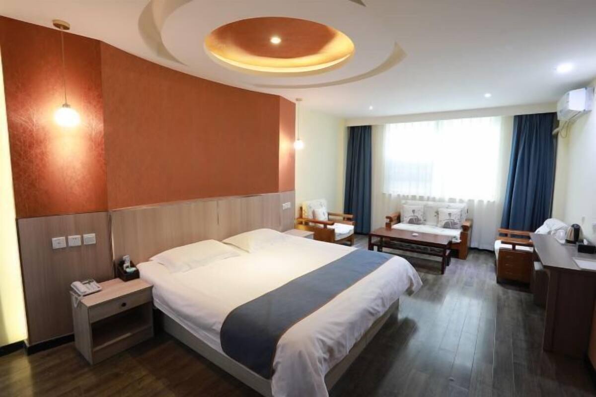 Une chambre d’hôtel avec un grand lit, un bureau, une chaise, une petite table, une table de chevet et une fenêtre avec des rideaux.