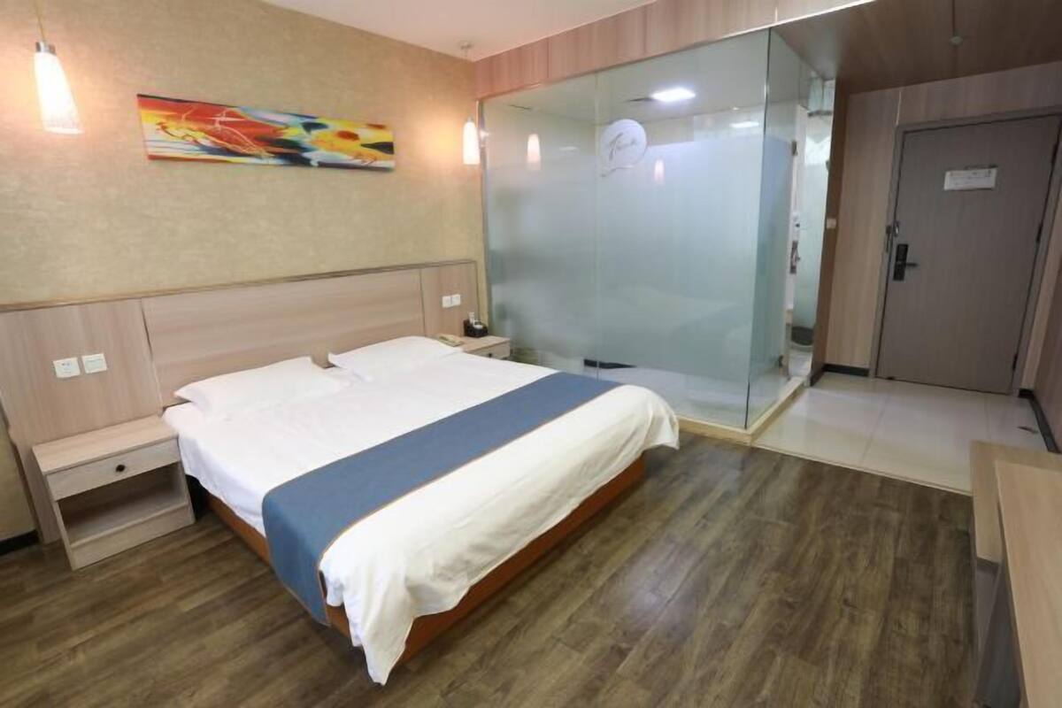Une chambre d’hôtel comprenant un lit, une table de chevet, une cabine de douche en verre et une armoire en bois.